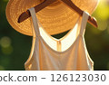 Summer casual dress and hat hanging on hanger in sunshine on green background, close-up 126123030