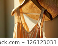 A yellow sundress hangs on a hanger on a white wall in the fitting room in a boutique, the rays of the sun fall on it 126123031