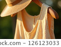 Woman's Dress And Straw Hat Hanging On Wooden Hanger On Green Background In Sunlight 126123033