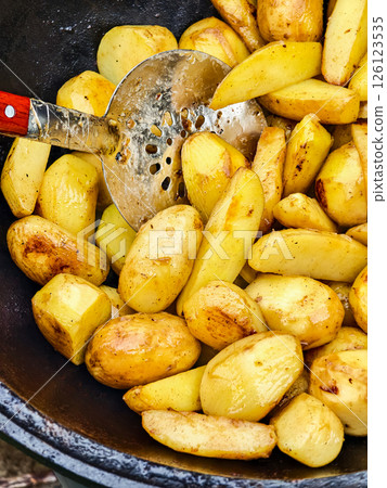 Golden roasted potatoes prepared in a rustic pot over a fire outdoors during an afternoon gathering 126123535