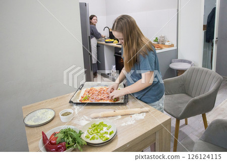 Cute child girl with woman cooking homemade pizza in domestic kitchen together. Mother and daughter 126124115