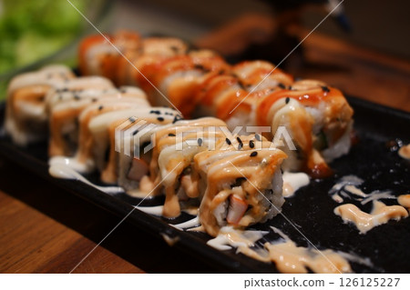 Sushi Rolls Topped with Creamy Sauces and Sesame SeedsSushi Rolls Topped with Creamy Sauces and Sesame Seeds 126125227