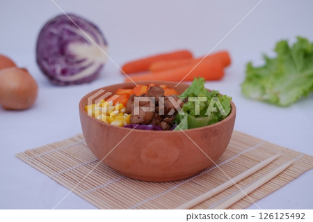 a colorful and appetizing bowl of food, placed on a bamboo mat with a pair of chopsticks beside it 126125492