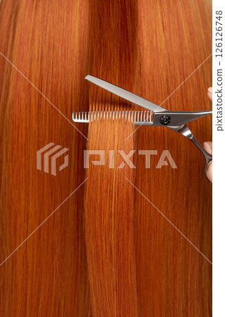 Hairdresser cuts long red hair with scissors Hairdresser cuts long red hair with scissors 126126748