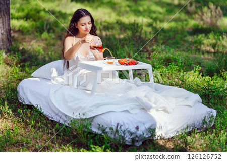 Young woman has breakfast in bed in a summer forest Young woman has breakfast in bed in a summer forest 126126752