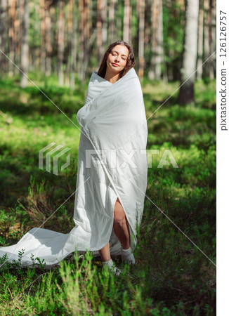 Woman stands in the woods wrapped in a blanket 126126757