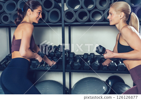 Two young women preparing for the workout with dumbbells in the gym 126126877