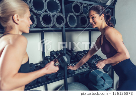 Two young women preparing for the workout with dumbbells in the gym 126126878