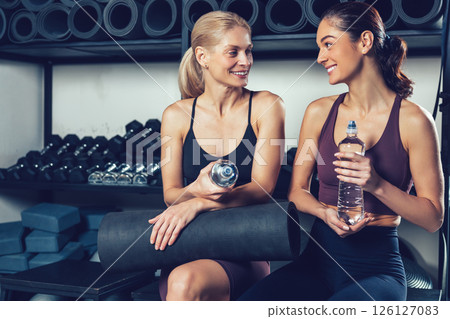 Two young women with water bottles in hands resting after exercising in the gym 126127083