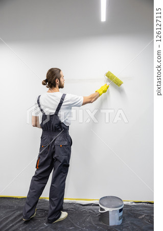 Young man in uniform painting the wall and looking busy 126127115