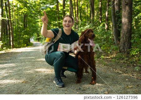 Smiling Woman with Map and Irish Setter Dog Exploring Forest Trail on Outdoor Adventure Smiling Woman with Map and Irish Setter Dog Exploring Forest Trail on Outdoor Adventure 126127396