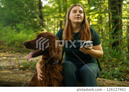 Woman Sitting on a Log with Her Dog in the Forest Woman Sitting on a Log with Her Dog in the Forest 126127401