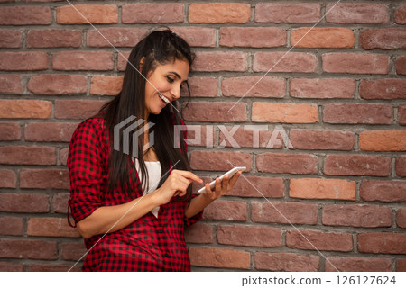 Smiling woman in red shirt looking at smartphone screen. 126127624