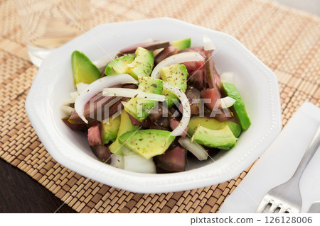 Salad of black tomatoes, avocado and onions in white ceramic bowl 126128006
