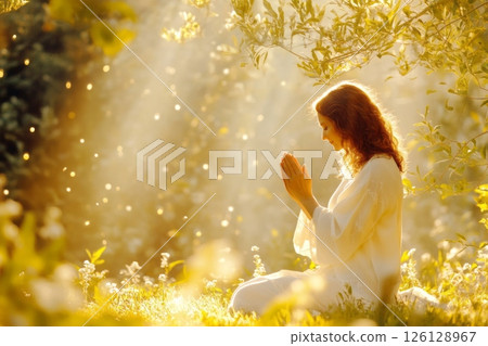 Woman praying in magical forest with golden light and floating particles 126128967