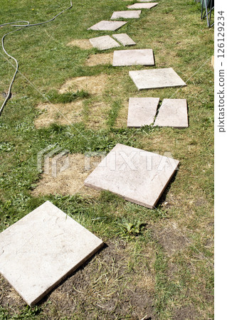Broken wonky paving slabs on grass that needs to be DIY finished Broken wonky paving slabs on grass that needs to be DIY finished 126129234