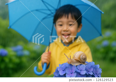 A boy smiles as he gazes at a snail on a hydrangea during the rainy season 126129523