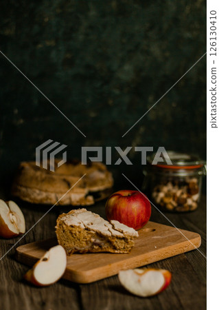Traditional apple pie Charlotte. Sliced apples lie nearby. Sweet Thanksgiving dinner, autumn seasonal apple pie slice one piece on wooden tray, on dark wooden background 126130410