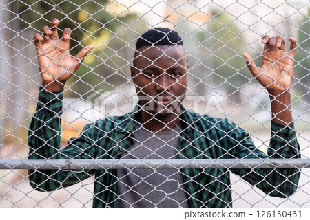 Aggressive African youth standing on the street behind the fence Aggressive African youth standing on the street behind the fence 126130431