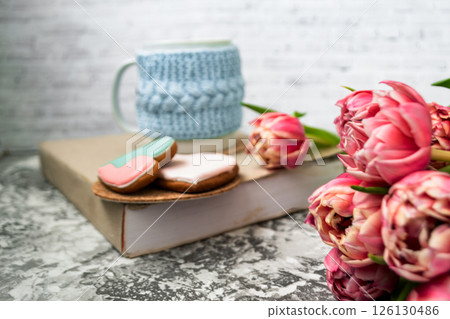 Pink tulips blurred foreground, open book and a mug of freshly brewed coffee or tea. Spring set. Pink tulips blurred foreground, open book and a mug of freshly brewed coffee or tea. Spring set. 126130486