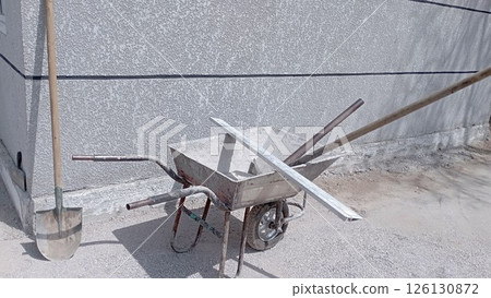 construction wheelbarrow-trolley rake, pitchfork inside. Shovel stands against the wall next to the wheelbarrow construction wheelbarrow-trolley rake, pitchfork inside. Shovel stands against the wall next to the wheelbarrow 126130872