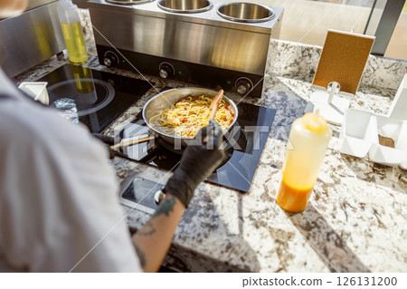 A skilled chef is cooking pasta in a modern kitchen with a stylish granite countertop 126131200