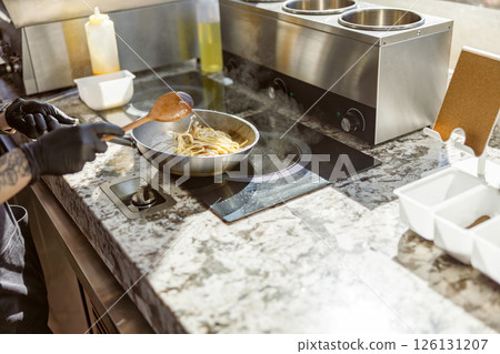 A chef is cooking delicious pasta in a modern kitchen, using quality cookware and fresh ingredients 126131207