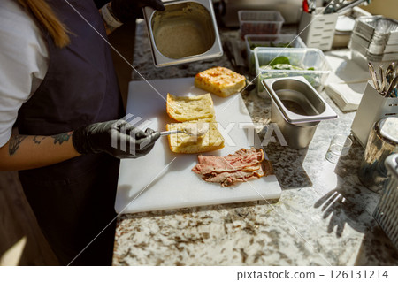 A skilled chef is making a delicious sandwich using the freshest ingredients in the kitchen A skilled chef is making a delicious sandwich using the freshest ingredients in the kitchen 126131214