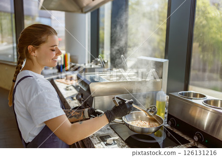 A Chef is skillfully Cooking in a Modern Kitchen, with Steam Rising from the Dishes 126131216