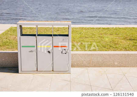 Trash can with three bins sits on a sidewalk next to a body of water. recycling. 126131540