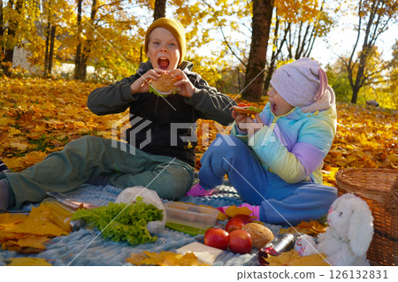 A boy and girl enjoy a delightful picnic in a public park on a sunny autumn day. Surrounded by vibrant fall foliage, they share snacks and laughter, embracing the warmth and beauty of the season. A boy and girl enjoy a delightful picnic in a public park on a sunny autumn day. Surrounded by vibrant fall foliage, they share snacks and laughter, embracing the warmth and beauty of the season. 126132831