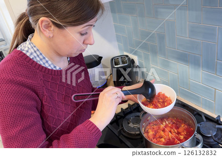 A woman in the kitchen puts borscht into a plate from a saucepan. A woman in the kitchen puts borscht into a plate from a saucepan. 126132832