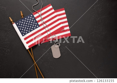 Military ID tag and USA American flags, symbolizing patriotism and honor. National pride and military tribute. Memorial and Veterans Day. View from above. Copy space. Military ID tag and USA American flags, symbolizing patriotism and honor. National pride and military tribute. Memorial and Veterans Day. View from above. Copy space. 126133155