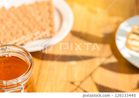 Orange Honey Jar on a Wooden Table With Wafers, Warm Sunlight Casting Shadows perfect for Cafes and Food Lovers 126133448
