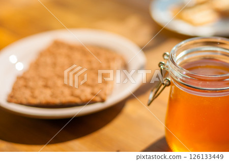 Honey Jar and Gingerbread Cookie on a Table, Warm Sunlight Creates a Cozy Cafe Vibe. Perfect for Bakeries Honey Jar and Gingerbread Cookie on a Table, Warm Sunlight Creates a Cozy Cafe Vibe. Perfect for Bakeries 126133449