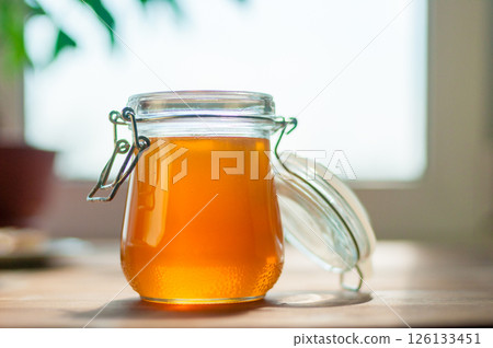 A Clear Glass Jar Filled With Golden Honey Rests on a Wooden Table A Clear Glass Jar Filled With Golden Honey Rests on a Wooden Table 126133451