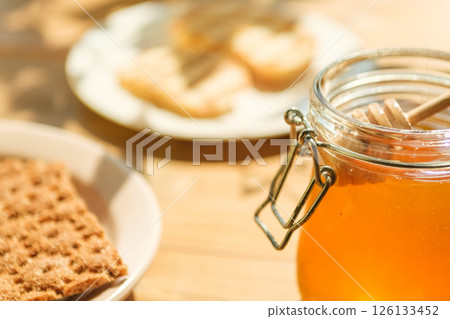Honey Jar With Wooden Dipper and Crackers on a Table, Sunlit; a Cafe and Culinary Arts Vibe Honey Jar With Wooden Dipper and Crackers on a Table, Sunlit; a Cafe and Culinary Arts Vibe 126133452
