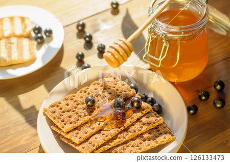 Honey Drizzled on Crackers With Berries on a Sunlit Wooden Table; Perfect for Food Bloggers and Gourmet Snack Lovers Honey Drizzled on Crackers With Berries on a Sunlit Wooden Table; Perfect for Food Bloggers and Gourmet Snack Lovers 126133473