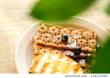 A Breakfast Platter Displays Whole Grain Crackers Drizzled With Honey, Garnished With Fresh Blueberries, Set on a Textured Cloth 126133489