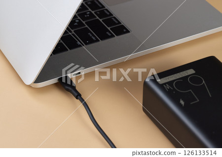 Charging laptop with power bank on beige background, close-up. 126133514