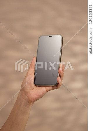 woman holding smartphone with blank screen on beige background, mockup 126133531