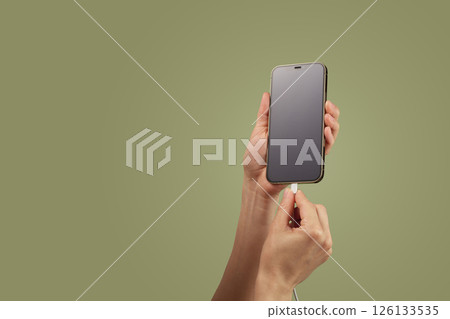 female hand plugging charger cord into smartphone to charge battery on green background, Wired charging female hand plugging charger cord into smartphone to charge battery on green background, Wired charging 126133535