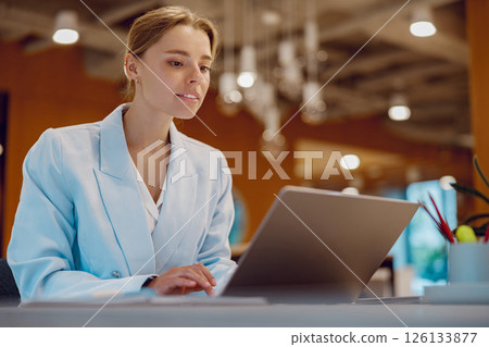 A professional woman is diligently working on her laptop within a modern office environment 126133877