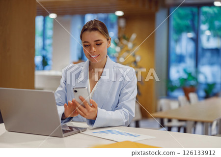 A professional woman is using her smartphone while working in a modern professional workspace A professional woman is using her smartphone while working in a modern professional workspace 126133912