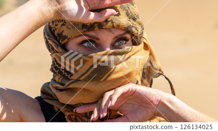 Woman with striking blue eyes in a desert scarf, covering her face from sand and sun. A mysterious Middle Eastern look 126134025