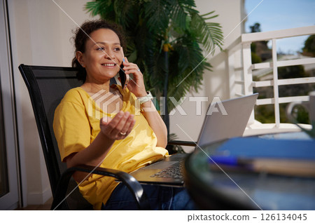 Woman in Yellow Shirt Having a Phone Conversation While Working on a Laptop Outdoors 126134045