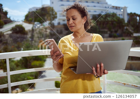 Female Professional Using Smartphone and Laptop on Balcony with Scenic View Female Professional Using Smartphone and Laptop on Balcony with Scenic View 126134057