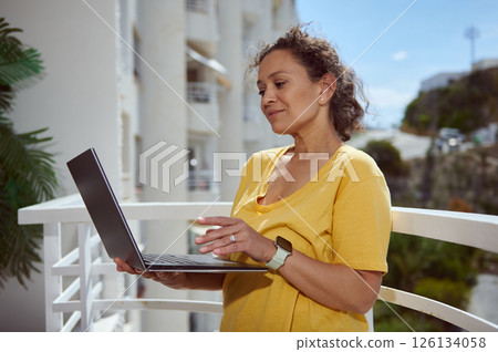 Woman in a Yellow Shirt Holding a Laptop Outdoors Gently Smiling 126134058