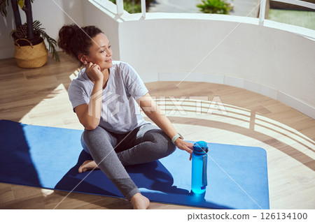 Woman Relaxing on a Yoga Mat After Exercise in a Bright Room 126134100