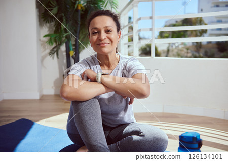 Smiling Woman Sitting in Activewear on Balcony Reflecting Relaxation and Fitness Smiling Woman Sitting in Activewear on Balcony Reflecting Relaxation and Fitness 126134101